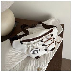 Detail of cream crossbody bag with brown zippers and elastic cord on wooden surface
