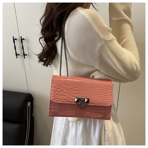 Detail of coral pink crocodile texture bag with dark grey metal chain on a model shoulder
