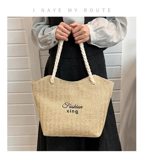 Close-up of herringbone weave straw tote bag featuring embroidered fashion text and rope handles