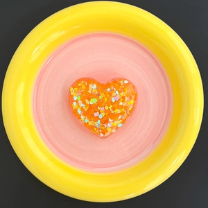 Detail of heart-shaped phone grip with vibrant orange and iridescent sequins inside