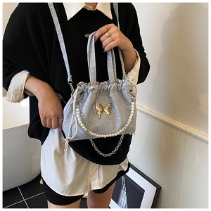 Detail of light blue bucket bag featuring gold butterfly buckle and pearl chain ornament
