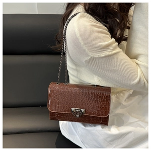 Close-up of brown crocodile texture flap bag with grey metal chain and clasp