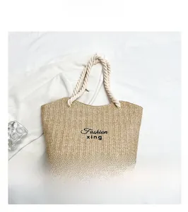 Detail of woven straw tote bag with rope handles and embroidered Fashion text on white