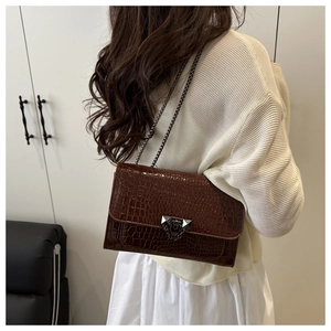 Deep brown crocodile pattern chain bag with metallic buckle shown in a lifestyle setting