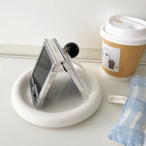 Detailed view of clear Samsung Z Flip case with a black spherical ring grip on a white plate
