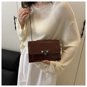 Close-up of a brown crocodile pattern crossbody bag with silver chain strap on model