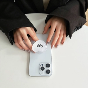 Detail of a white heart phone grip with a black bow on a smartphone in hand