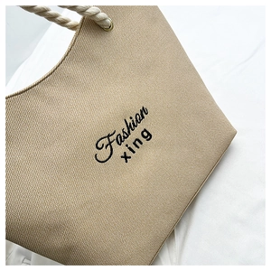 Detail of beige woven tote bag showing texture, cotton rope handle and black embroidery