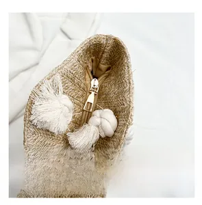Detailed view of the straw tote bag showing the smooth gold metal zipper and white tassels