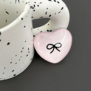 Macro detail of a pink heart-shaped phone grip featuring a black bow design