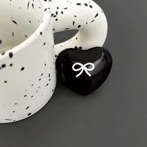 Macro shot of heart-shaped black phone grip with white bow pattern on textured ceramic cup