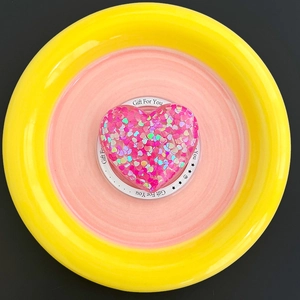 Macro shot of glitter-filled pink heart MagSafe phone grip in a colorful ceramic plate