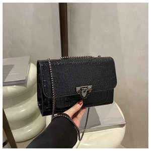 Detailed view of black crocodile pattern leather bag with silver chain strap and metal lock