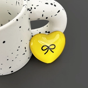 Macro shot of yellow heart phone grip with black bow print on white textured cup