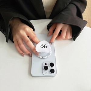 Macro detail of a heart-shaped phone grip with a black bow pattern on a white smartphone