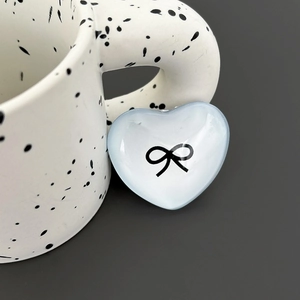 Close-up of a light blue heart-shaped phone grip with a black bow print on a ceramic cup