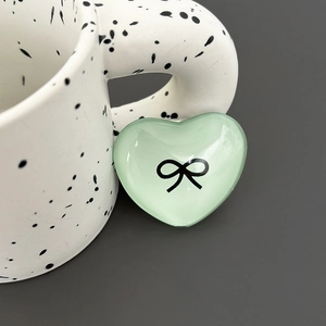 Close-up of heart-shaped light green phone grip with a black bow pattern on a ceramic mug