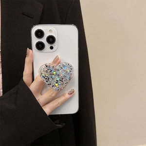 Detail of a heart-shaped phone grip with silver glitter on a white smartphone