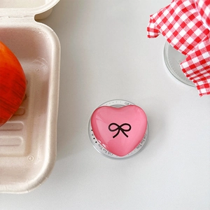 Pink heart phone grip with black bow on a white desk with aesthetic props