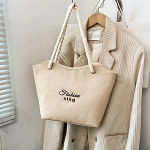 Beige canvas tote bag with thick rope handles and black embroidery on a corduroy jacket