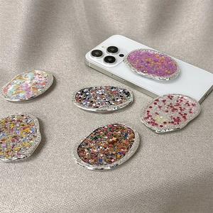 Glittery oval phone socket grip with silver scalloped edges on white smartphone