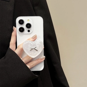 Detail of a pearl heart phone grip with silver bow accent on a white smartphone
