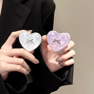 Detail view of heart-shaped phone grip with silver bow and pearlescent finish