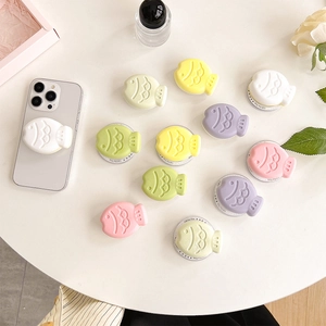 Colorful fish-shaped macaron phone grip stands displayed on a stylish white desk