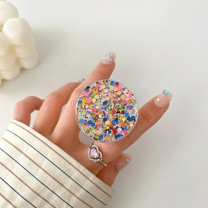 Close-up of a round glitter phone socket with stars and sequins on a user's hand