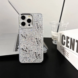 Detailed view of silver sequin iPhone case with metallic 3D heart charms on a desk