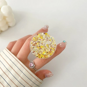 Detail of round phone socket with yellow glitter sequins held by hand with heart ring