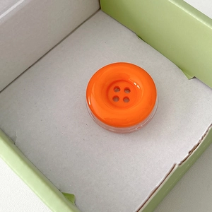 Macro shot of bright orange candy button retractable phone grip with four-hole design
