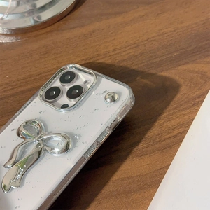 Dettaglio custodia iPhone 16 Pro Max con fiocco argento e glitter su sfondo bianco