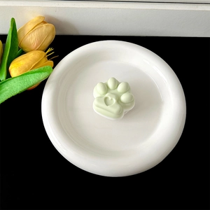 Detailed view of a cute light green cat paw phone grip placed on a white ceramic plate.