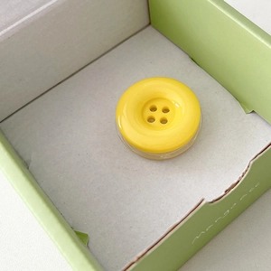 Macro shot of yellow button-shaped phone grip stand in a light green gift box