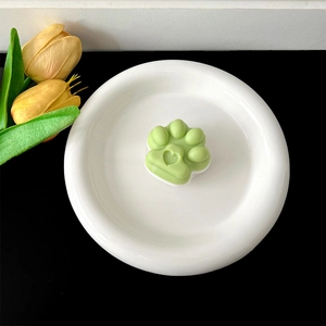 Close-up detail of a green cat paw collapsible phone grip resting on a white ceramic plate.