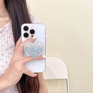 Detail of a heart-shaped glitter phone grip with blue and silver sequins on a white phone