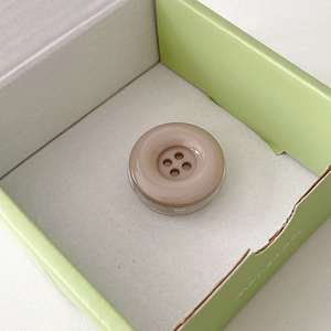 Macro detail of a beige candy-colored button phone socket grip on minimalist packaging