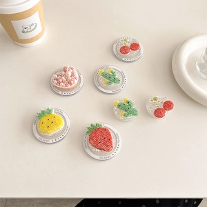 Detailed close-up of colorful acrylic fruit phone grips with decorative beads on a desk