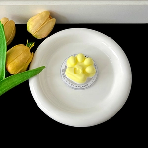 Macro detail of a cute yellow and white cat paw shaped phone grip stand on a white plate