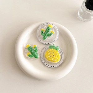 Detailed view of cactus and pineapple phone grips displayed on a white ceramic plate