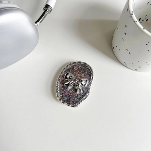 Detail view of oval glitter phone grip featuring a silver 3D bow and starry shimmer