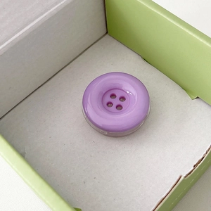 Detail view of a purple candy button phone grip with a cute 4-hole resin design in a box