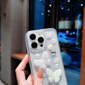 Détail d'une coque iPhone transparente avec papillons nacrés, perles et breloques de cœur
