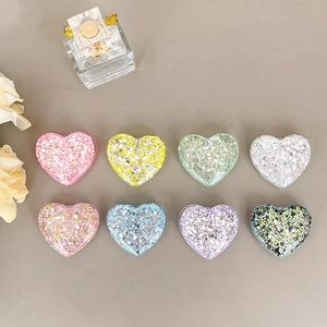 Eight colorful glitter heart-shaped phone grips with sequins on a clean desktop background