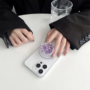 Close-up of a purple heart-shaped glitter phone grip with Gift For You text on white iPhone