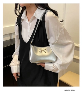 Detail of silver metallic underarm bag with a gold bow buckle on a fashion model