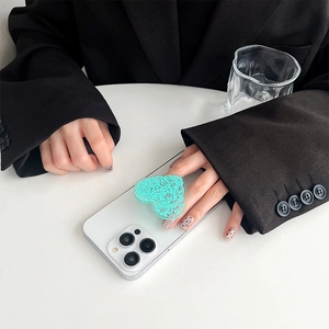 Detailaufnahme der glitzernden Herz-Handyhalterung in Minzgrün auf weißem Smartphone