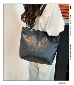 Close-up of black crocodile-embossed tote bag with gold chain strap worn by a model