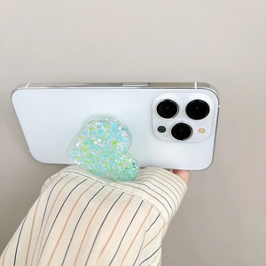 Close-up of heart-shaped phone grip with teal glitter sequins on a white smartphone